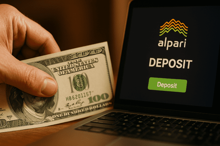 Close-up of hand holding US 0 bill next to laptop screen showing Alpari deposit button and logo